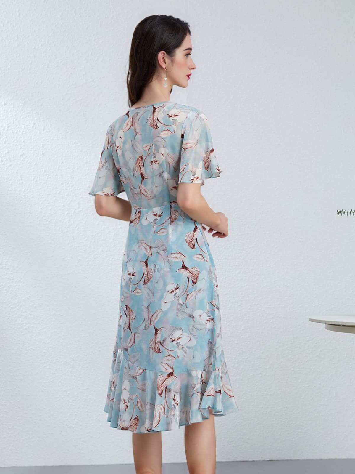 Back view of a woman wearing a Blue Floral Mulberry Silk Dress with short sleeves and a ruffled hem.