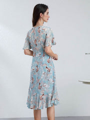 Back view of a woman wearing a Blue Floral Mulberry Silk Dress with short sleeves and a ruffled hem.