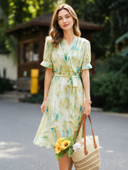 A woman wearing a Resort Style Mulberry Silk Dress with floral prints, holding a tote bag and sunflowers, outdoors.