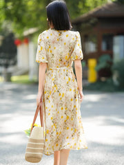 Model wearing a French Floral Mulberry Silk Maxi Dress with puff sleeves, holding a tote bag, outdoors in a sunny setting.