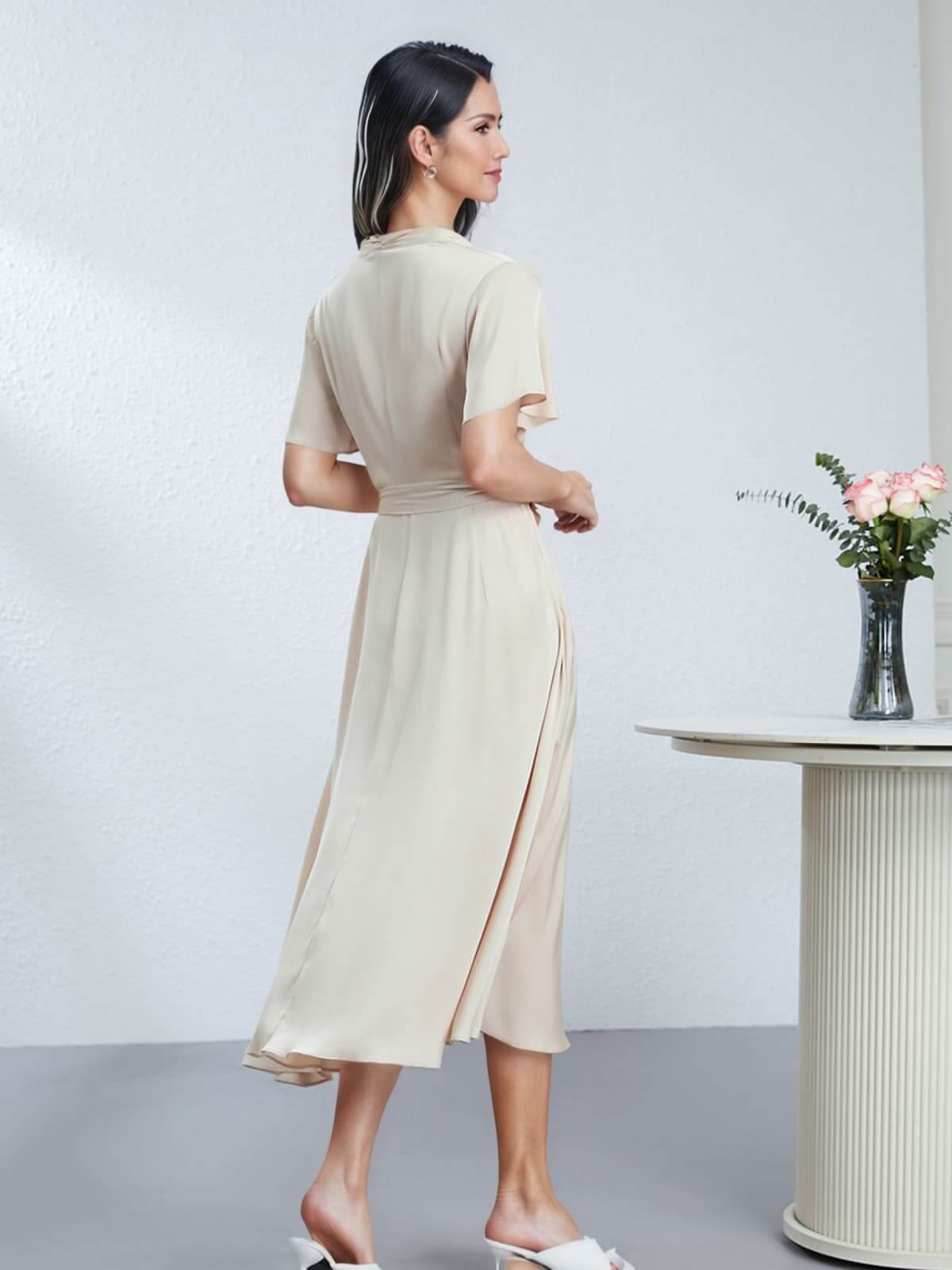 Back view of a woman wearing a Heavyweight Ruched Waist Mulberry Silk Maxi Dress, standing beside a vase of flowers.