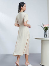 Back view of a woman wearing a Heavyweight Ruched Waist Mulberry Silk Maxi Dress, standing beside a vase of flowers.