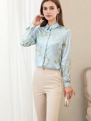 Woman wearing a Floral Long Sleeve Mulberry Silk Blouse, pairing it with cream pants, standing by a window.