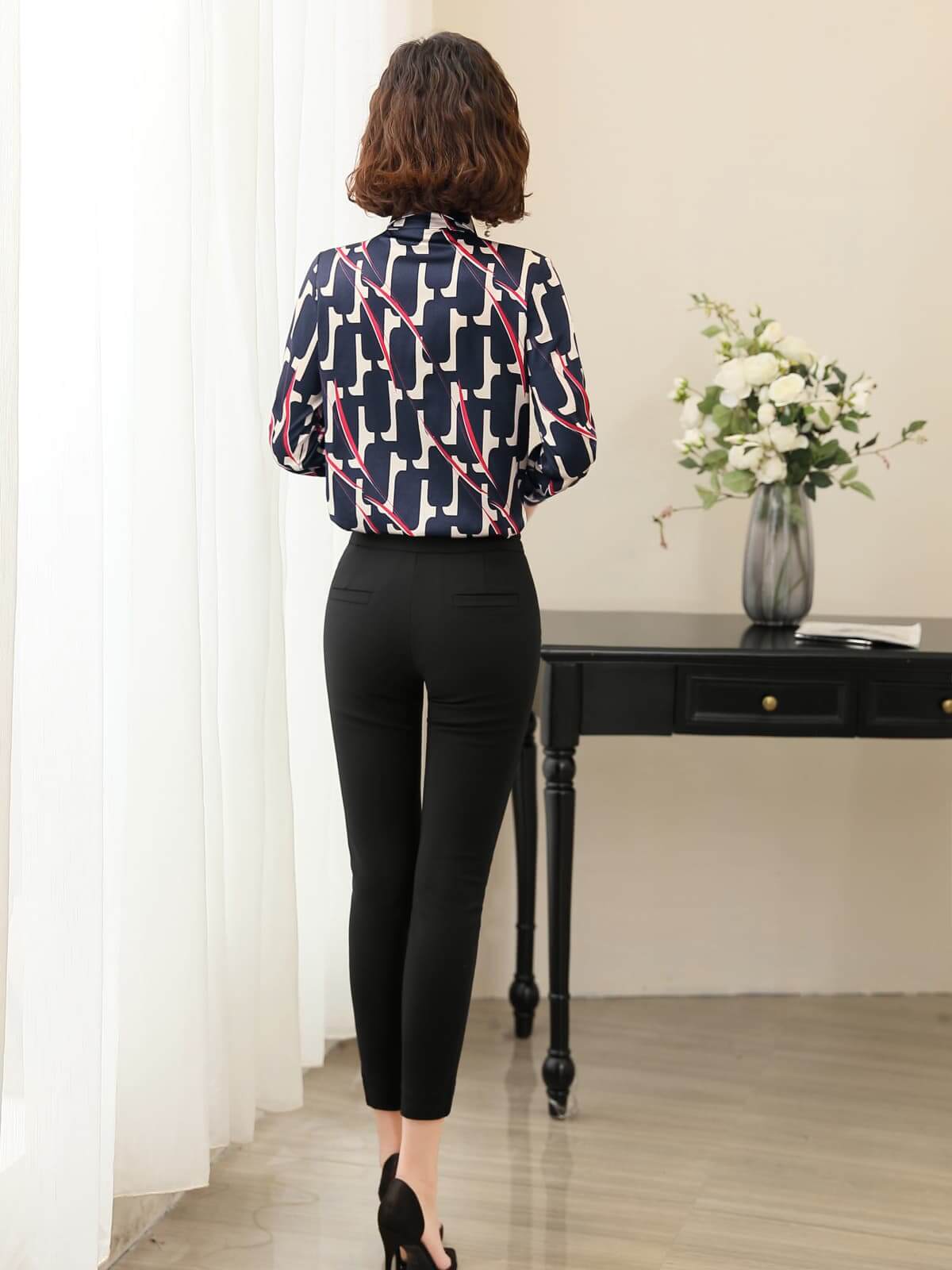 Back view of a woman wearing a Luxury Printed Mulberry Silk Blouse paired with black pants in a stylish setting.