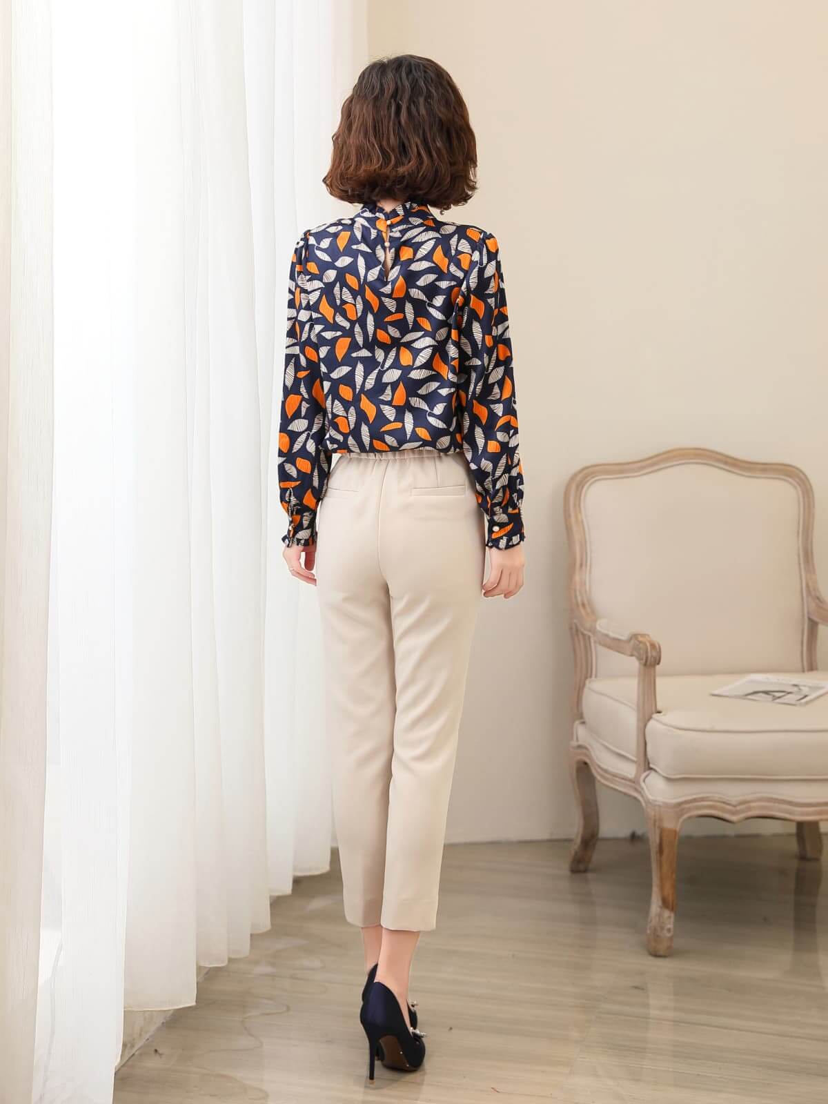 Woman wearing a Vintage Floral Mulberry Silk Blouse, viewed from the back, paired with beige trousers in a stylish setting