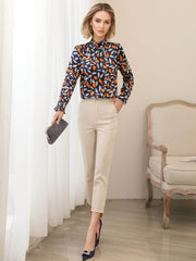 Woman wearing a stylish Vintage Floral Mulberry Silk Blouse paired with cream trousers, standing elegantly by the window.