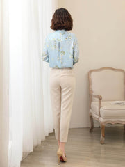 Woman wearing a Floral Long Sleeve Mulberry Silk Blouse, pairing it with cream pants, standing by a window.