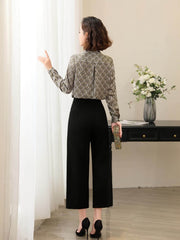 Back view of a woman wearing a Floral Long Sleeve Mulberry Silk Blouse with black pants in a bright room.