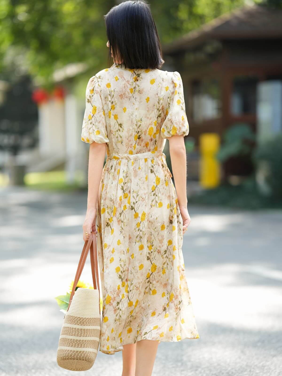Model wearing a French Floral Mulberry Silk Maxi Dress with puff sleeves, holding a tote bag, outdoors in a sunny setting.
