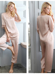 Woman wearing a pink silk pajama set in a room with white walls.